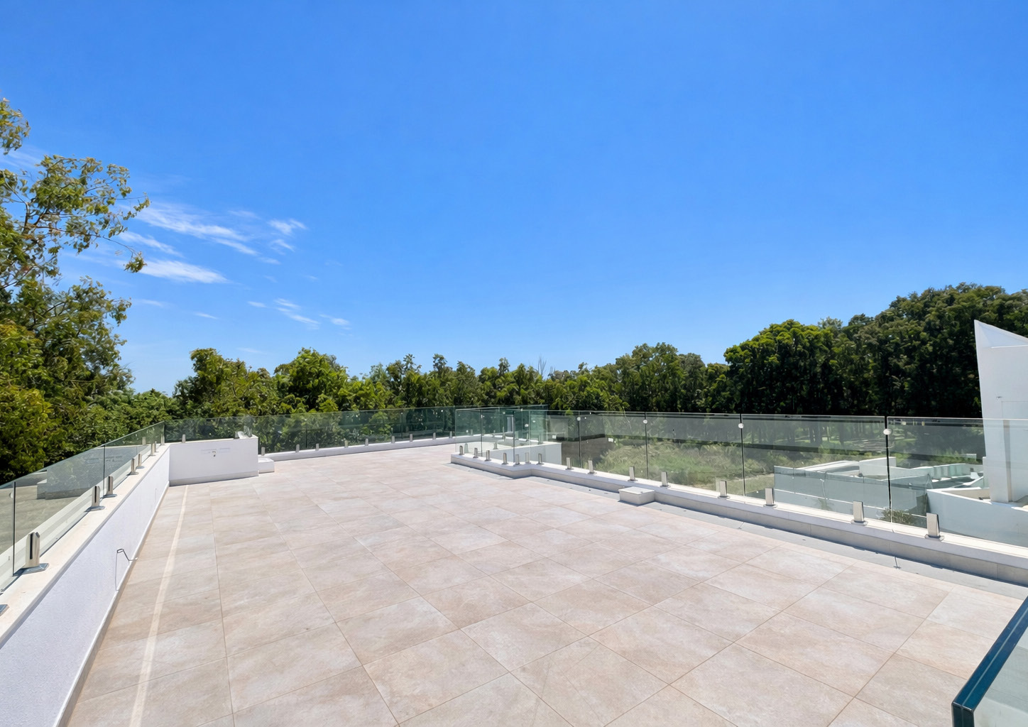 The roof terrace, paved in pale stone behind a glass balustrade, with trees beyond. Villa Dunas, Nueva Atalaya, Estepona.