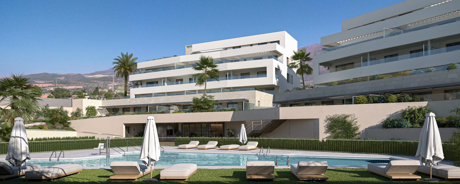 A pool at the foot of the buildings, with sun loungers on the lawn and the mountains behind. Zenity Blau I, La Gaspara, Estepona.