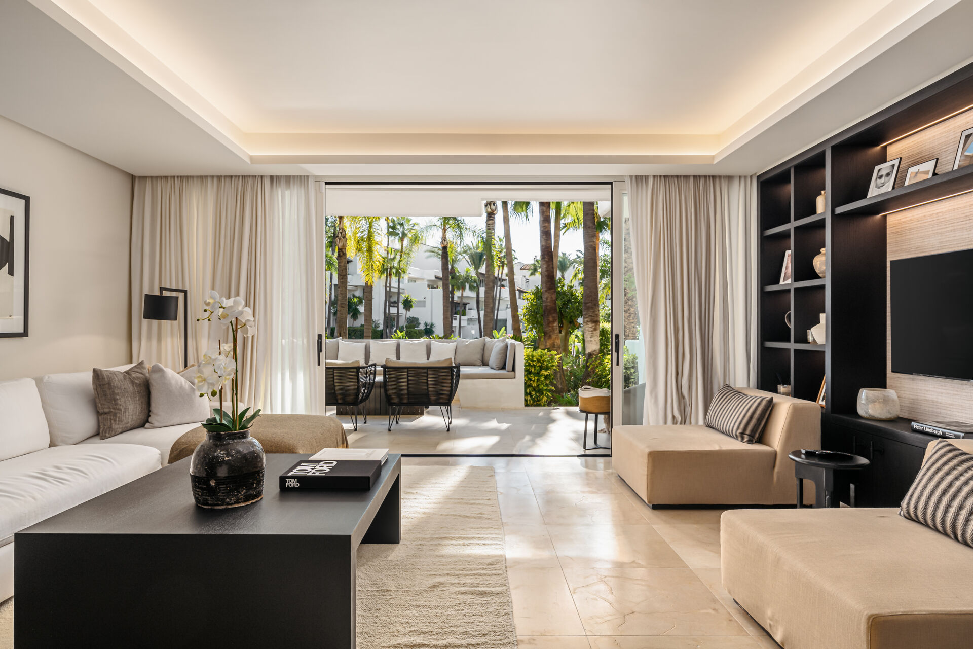 The living room, with its glass doors open onto the terrace and the palms of the gardens beyond.