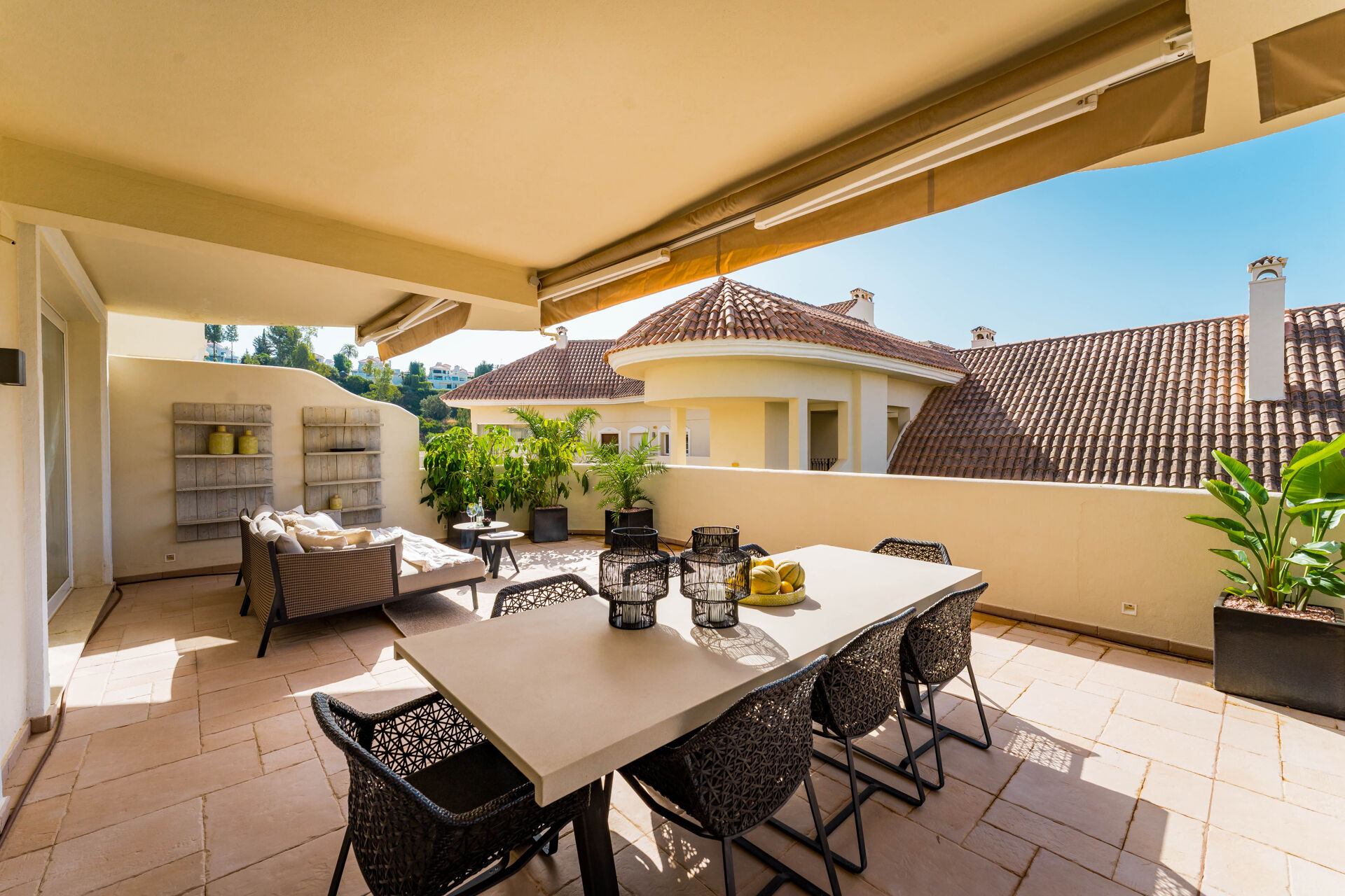 The dining table and woven chairs on the terrace, under an awning, beside the tiled roofs of the neighbouring buildings.