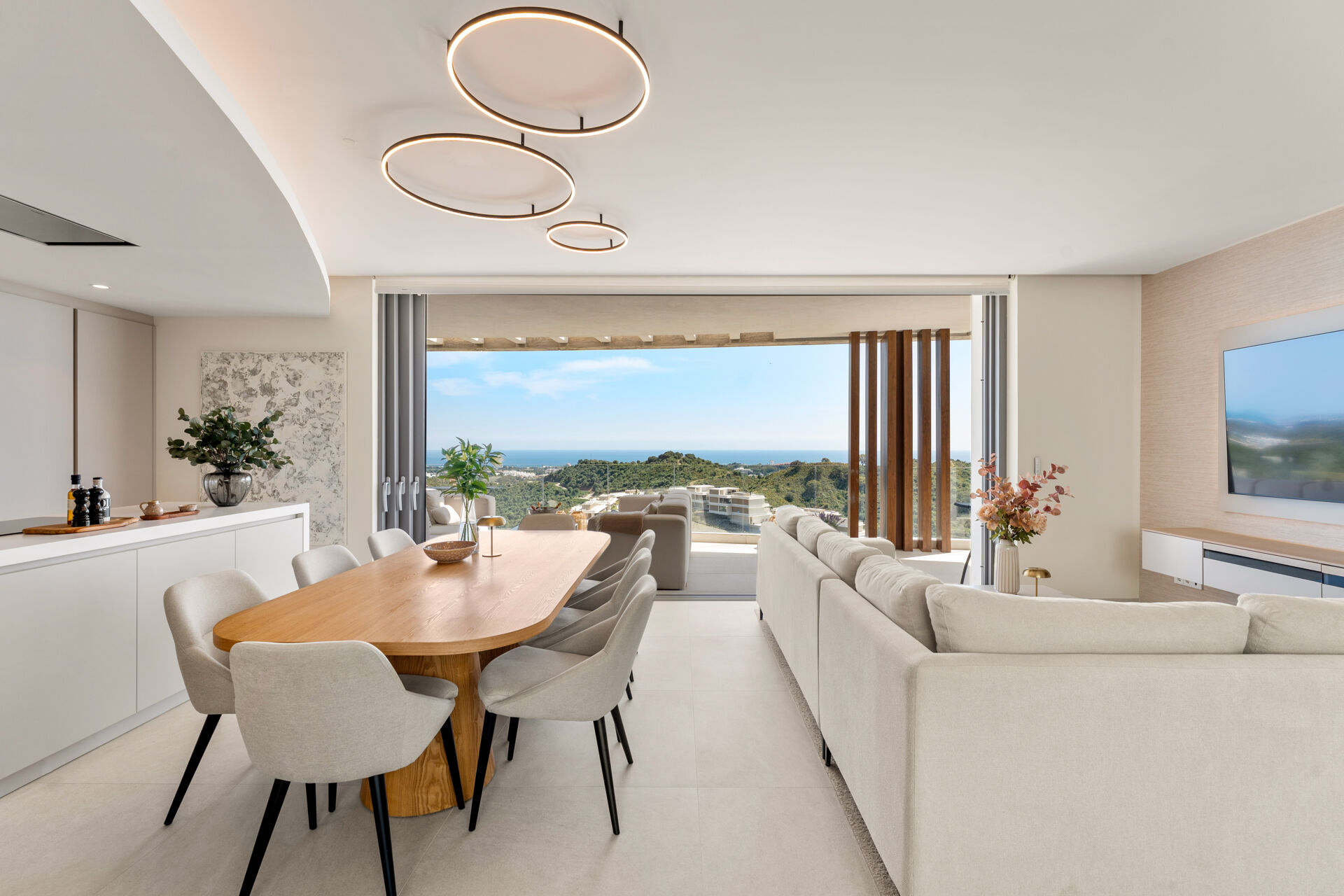 The oval dining table and the living area, with the glass doors open onto the terrace and the sea in the distance.