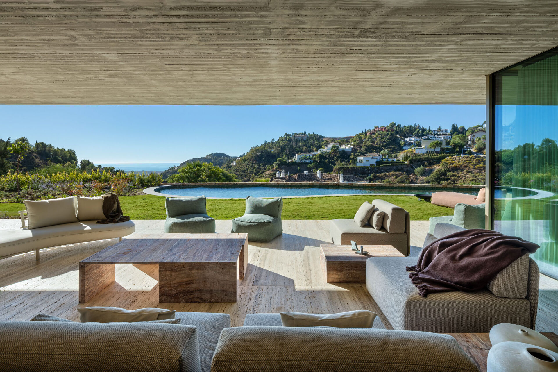 The covered terrace outside the living room, looking across the lawn and the pool to the hills and the sea.