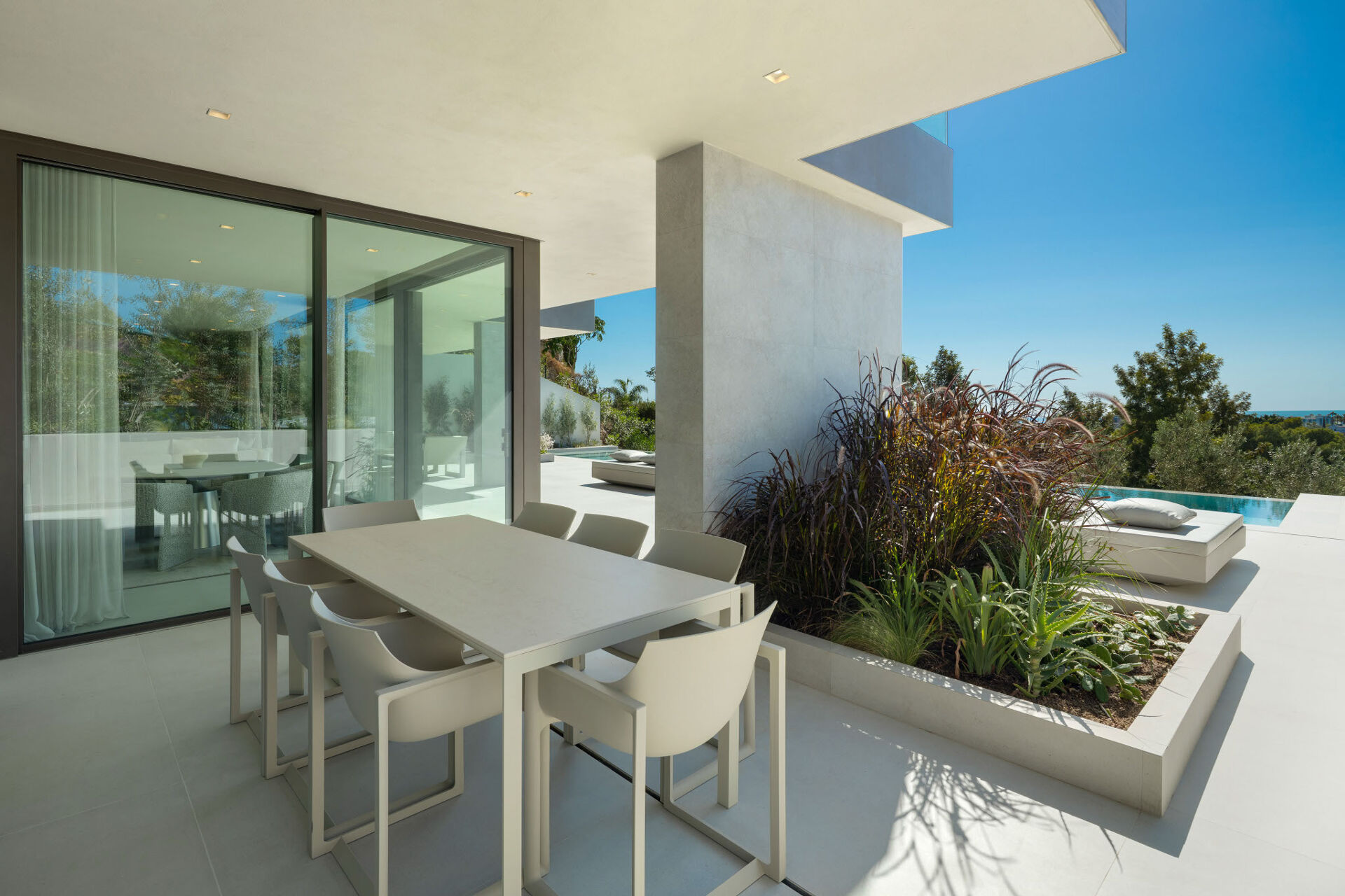 The covered terrace, with an outdoor dining table beside the glass doors, a daybed and the edge of the pool beyond.