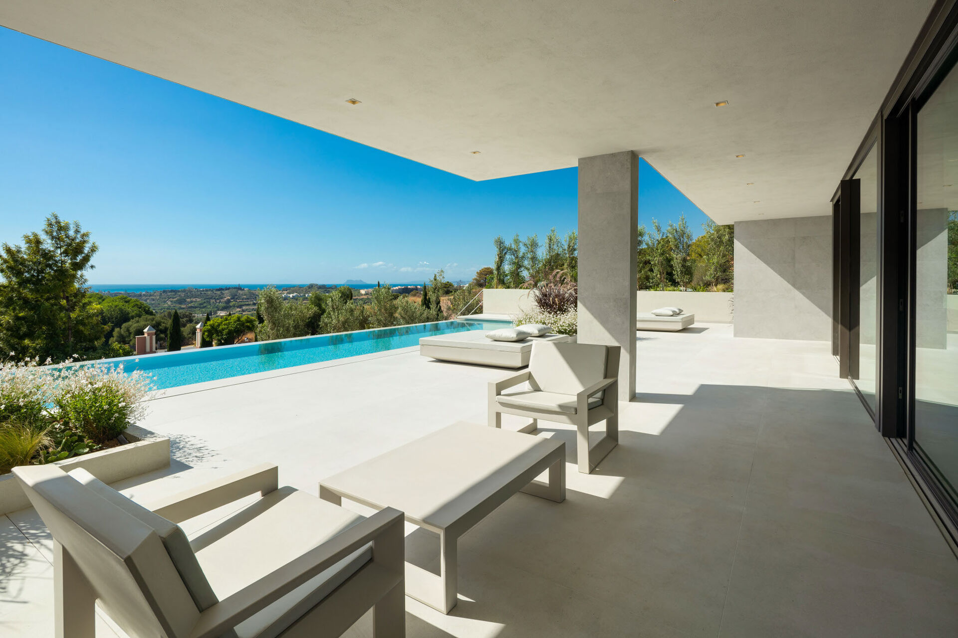 The covered terrace, with outdoor seating and daybeds beside the infinity pool, and the sea on the horizon.
