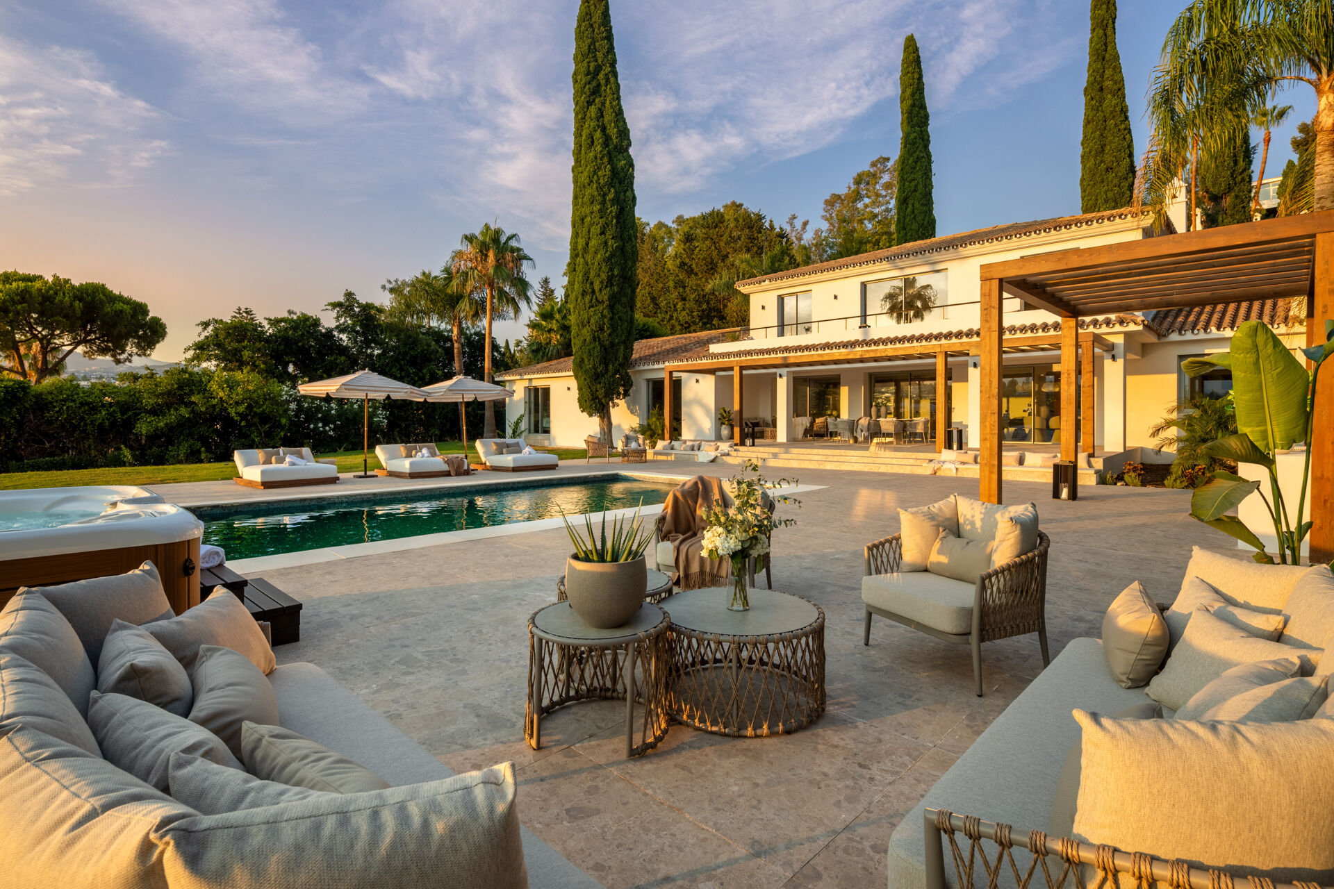 The covered terrace and the swimming pool on the garden side of the villa, with sun loungers on the lawn.