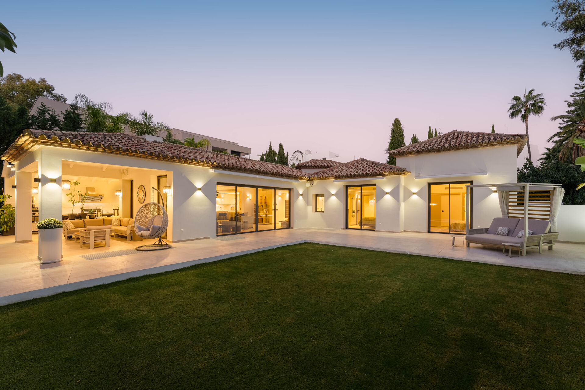 The villa at dusk with its lights on, seen across the lawn, with the covered terrace on the left.