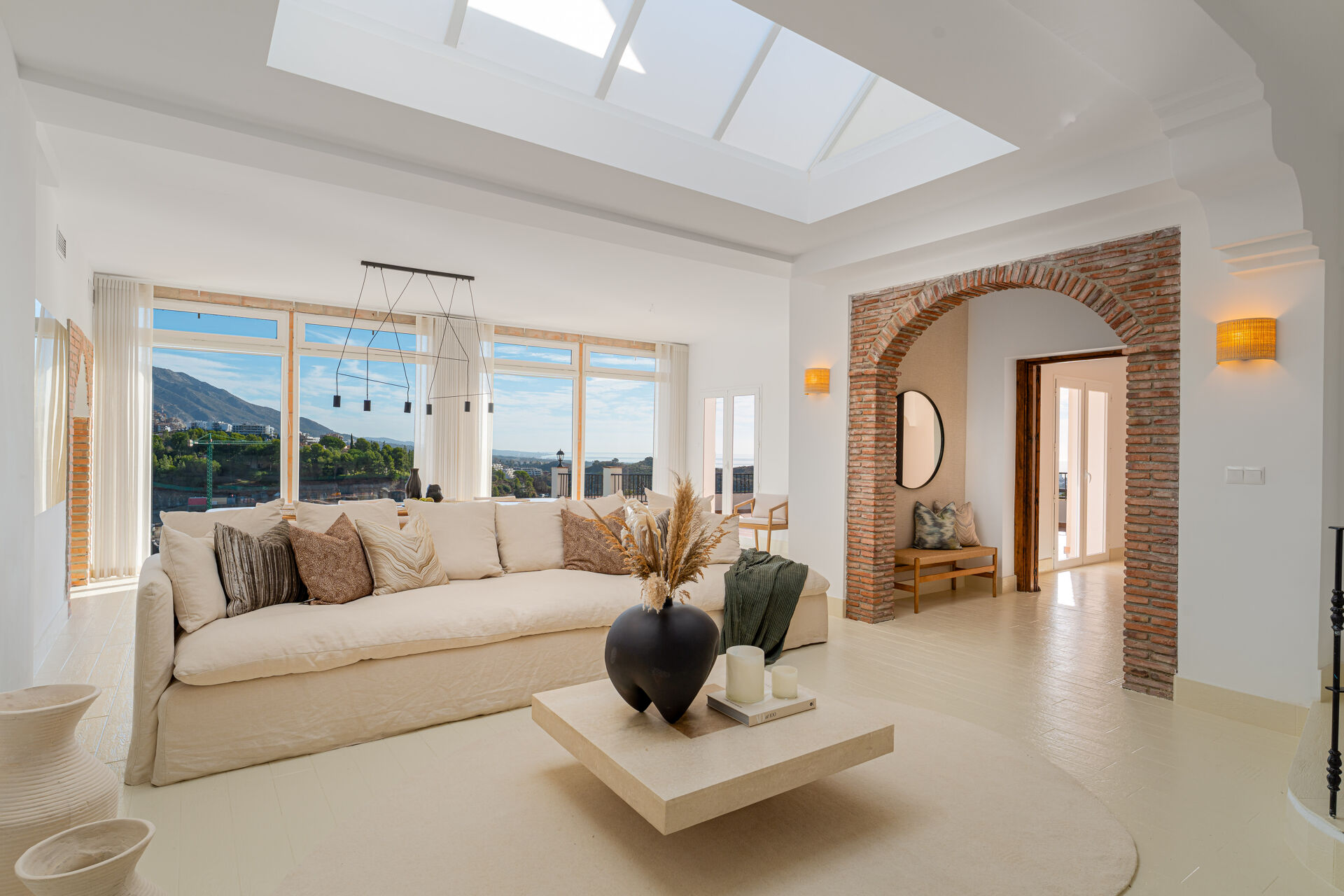 The living room, with a large sofa under a glass skylight and a brick arch through to the hall.