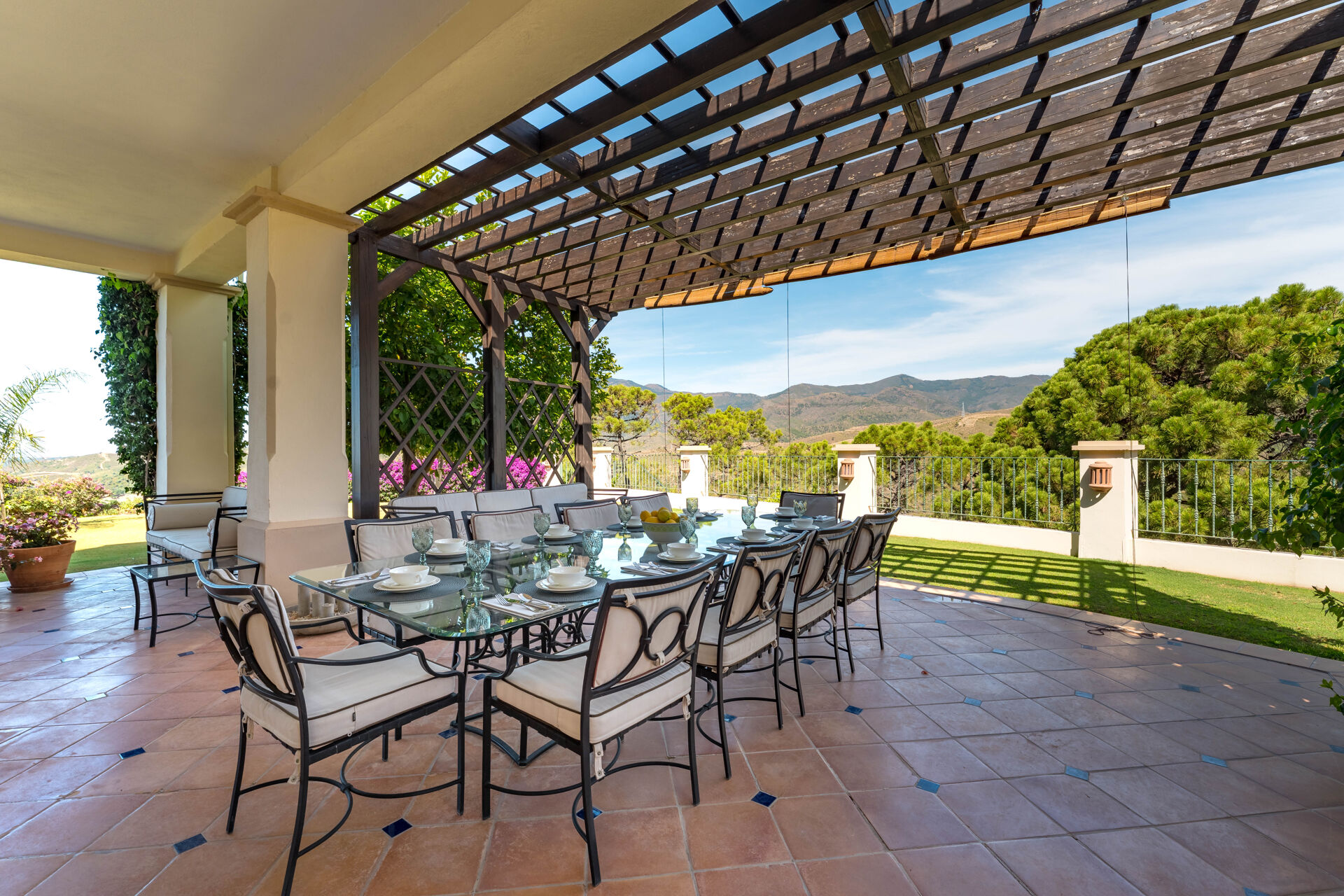 The covered dining terrace under a pergola, with the table laid for ten and the mountains beyond.