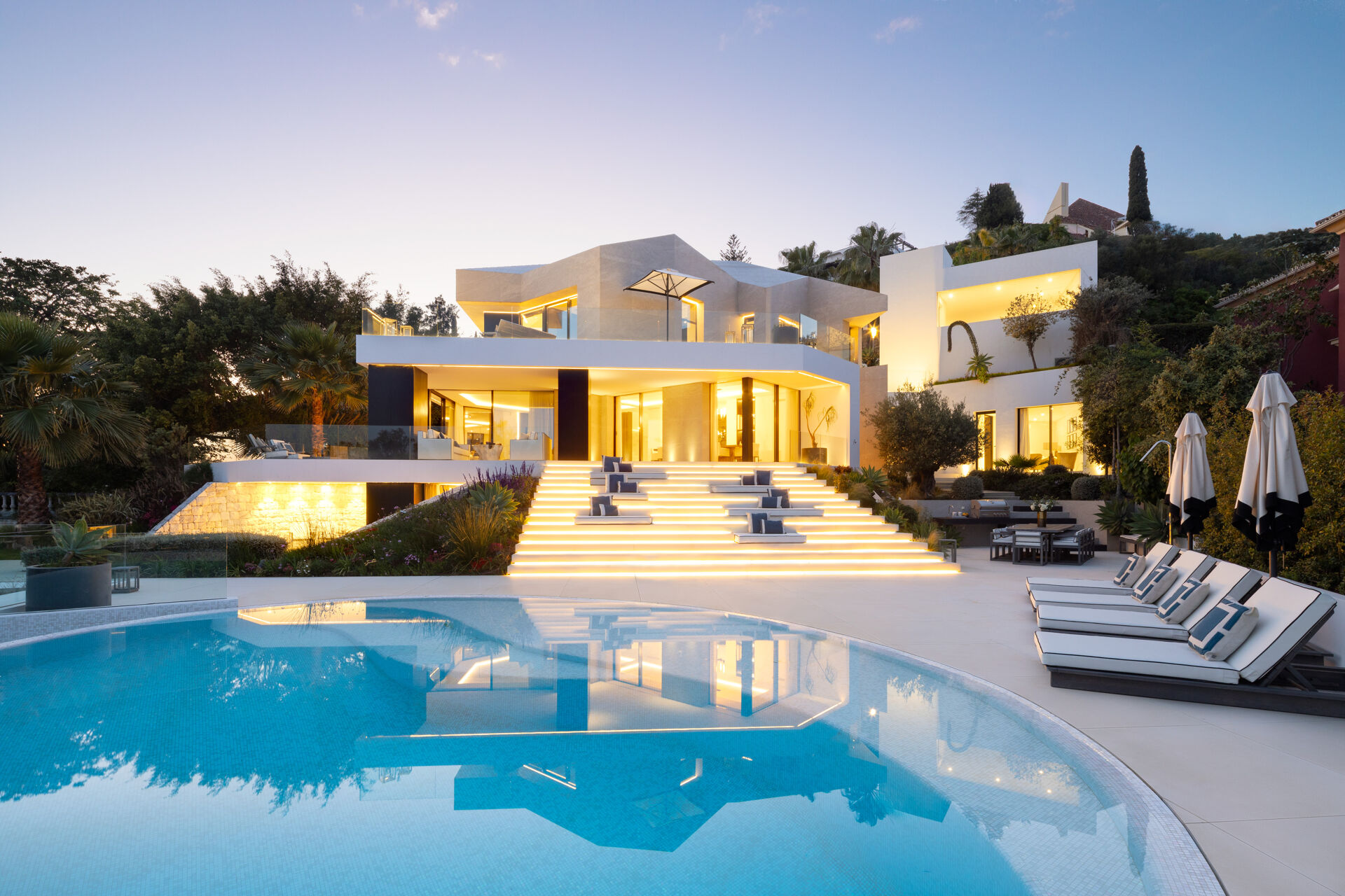 The villa at dusk, seen across the curved swimming pool, with the lit steps leading up to the terrace.