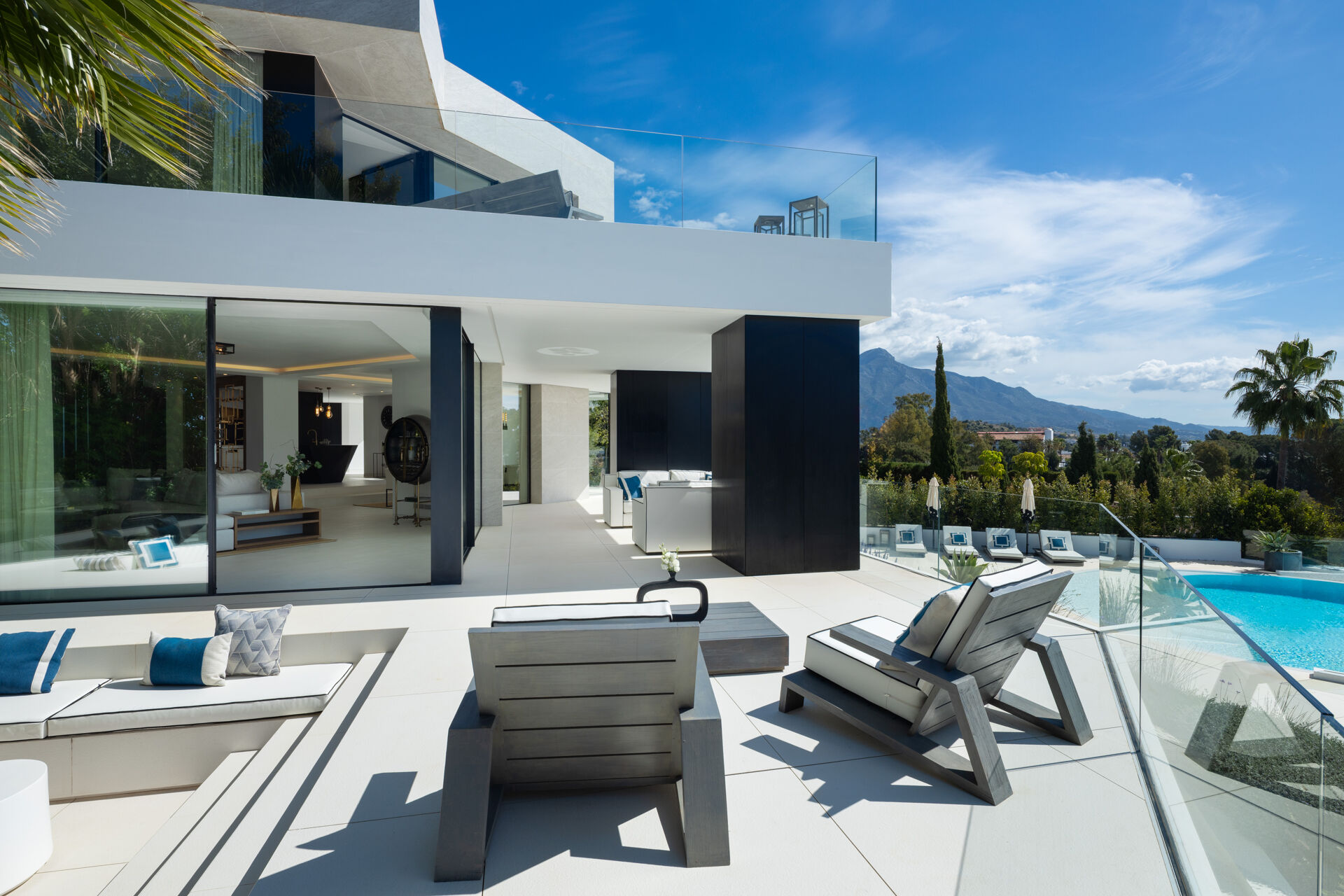 The terrace beside the living room, with sunken seating and loungers, the pool to the right and a mountain in the distance.