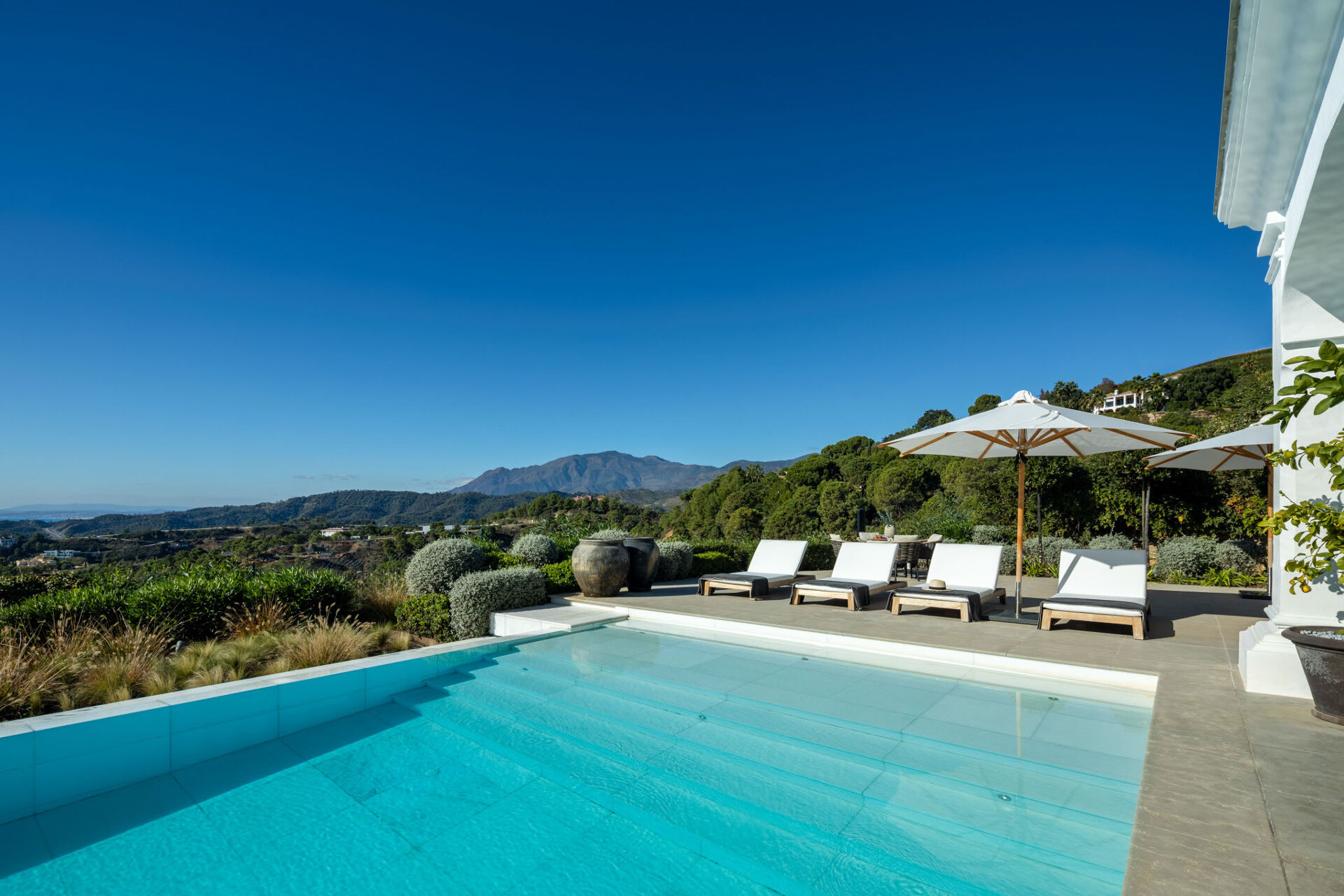 The swimming pool and sun loungers on the terrace, with wooded hills and a distant mountain beyond.
