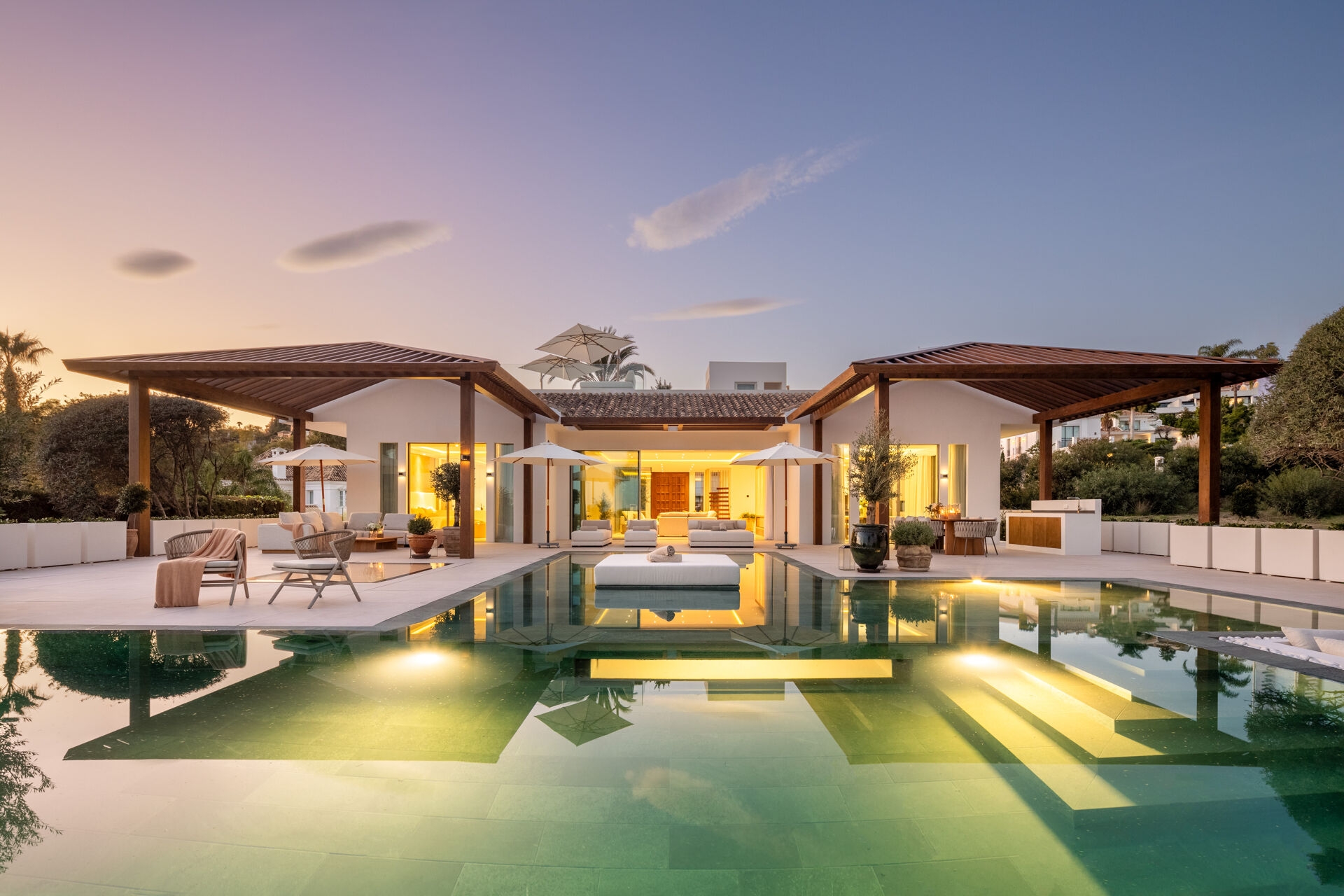 The swimming pool and the covered terraces at dusk, with the villa lit from inside.