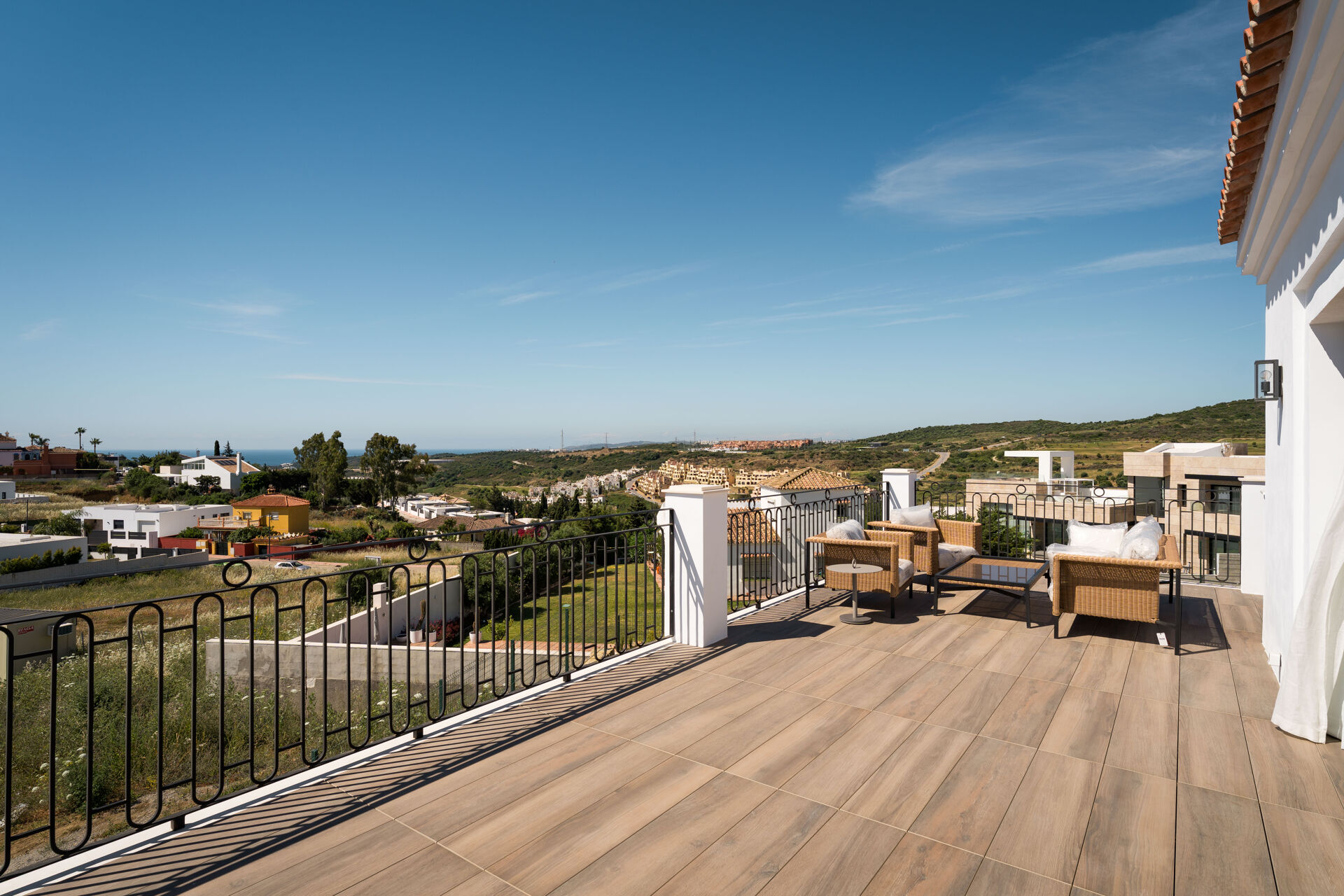 The upper terrace, with wicker seating and a view over the neighbouring houses and green hills to the sea.