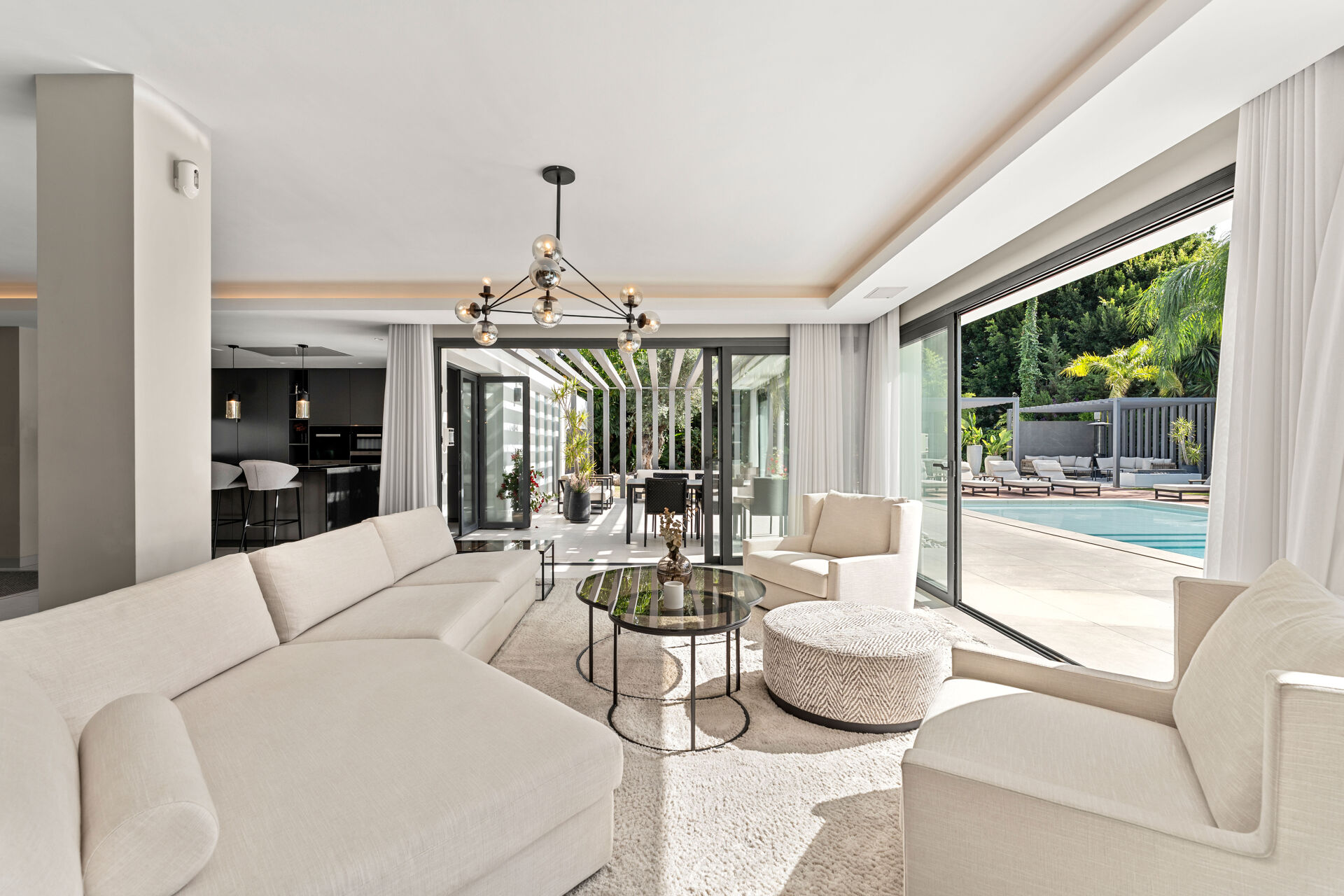 The living room, with a large corner sofa and armchairs, and sliding glass doors open to the covered terrace and the pool.
