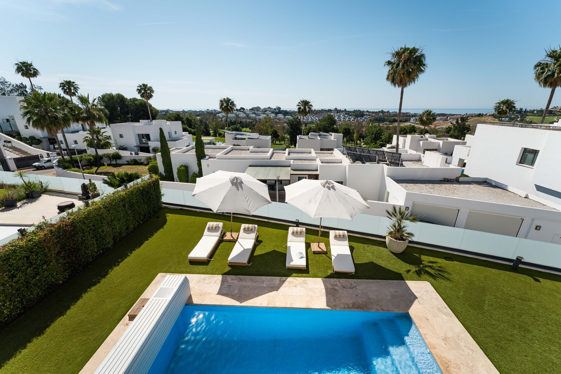 The view from an upper level over the pool and the lawn, towards a golf course and the sea on the horizon.