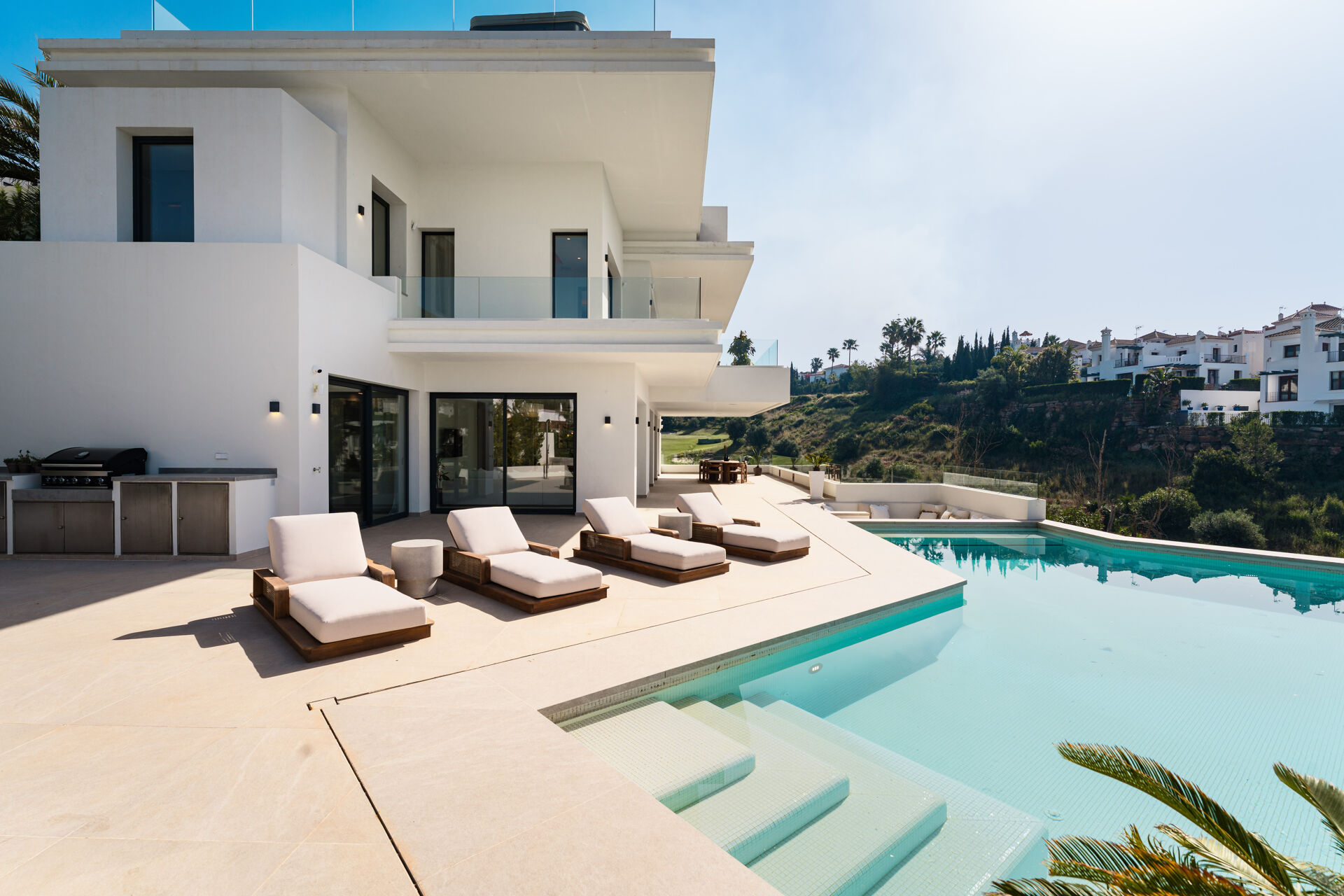 The swimming pool, the sun loungers and the built-in barbecue on the pool terrace, with a fairway of the golf course in the distance.
