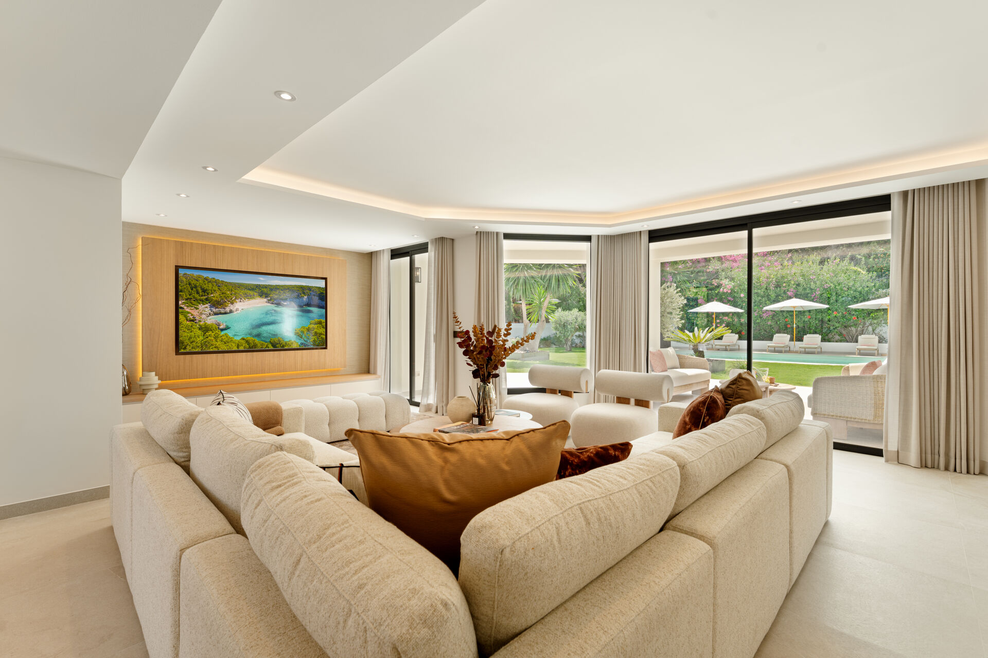 The living room, with a large corner sofa, a television wall and glass doors out to the garden.